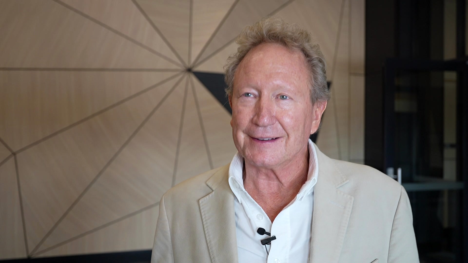 A man in a beige suit speaks to a camera