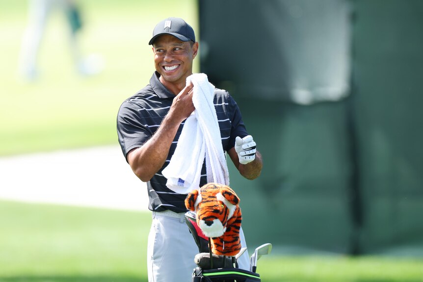 Tiger Woods smiles while holding a towel next to his golf bag at practice