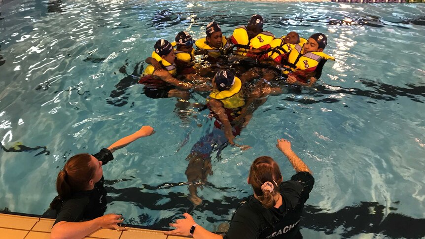 Migrant students wearing life jackets and clustered together in the pool.