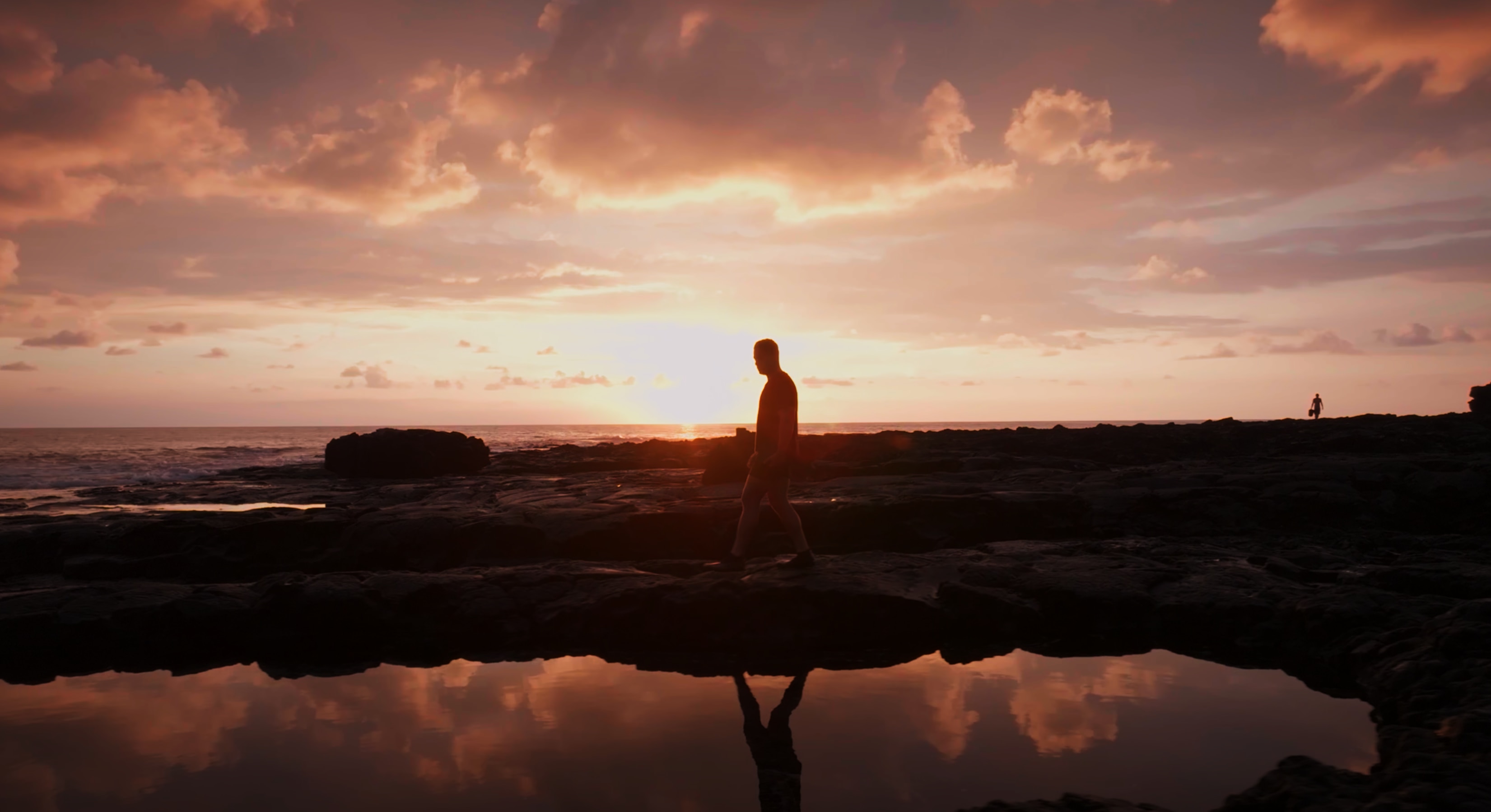 Marc walks over rocks at sunset in a Hawaiian bay.