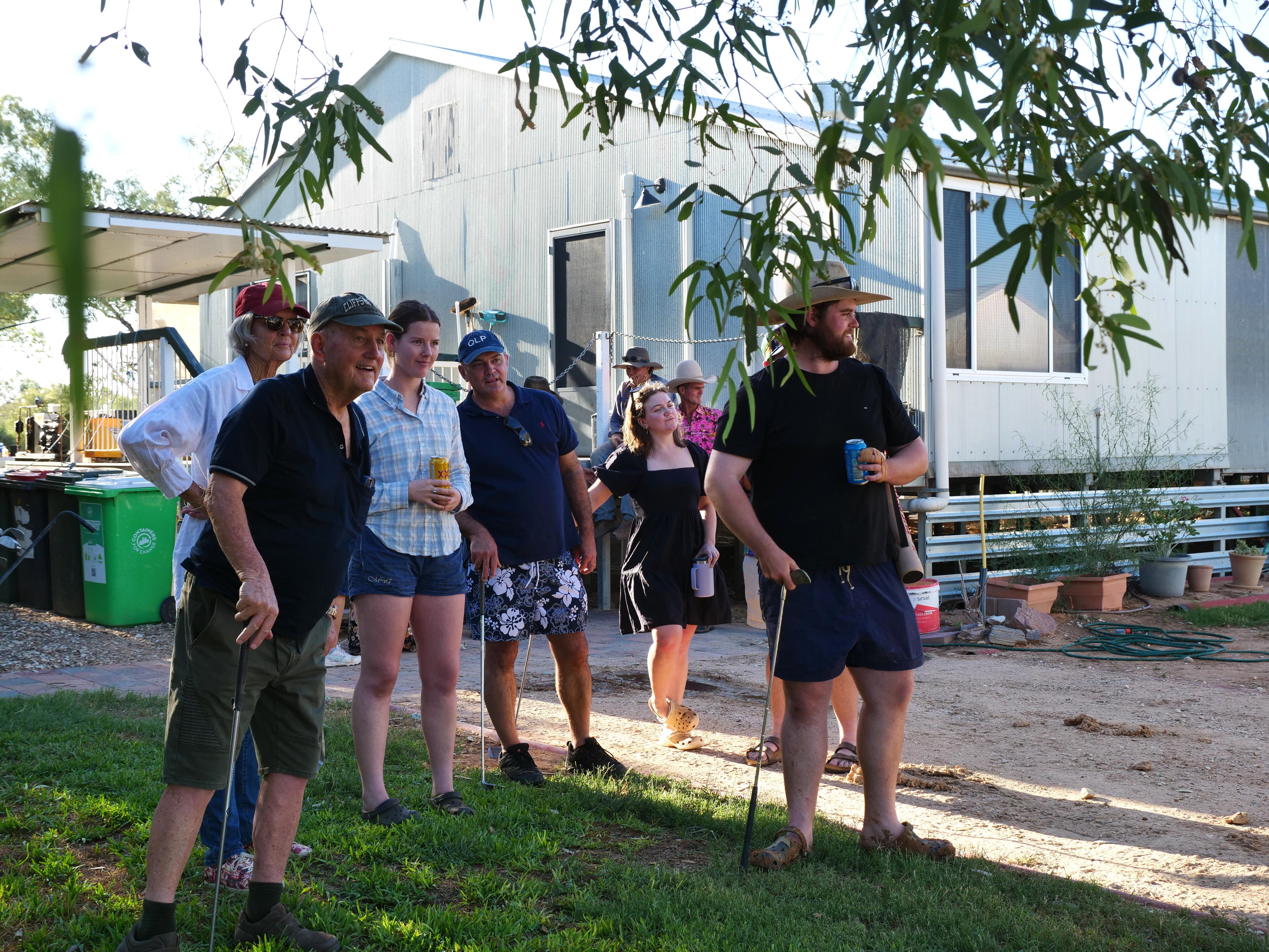 Um grupo de pessoas segurando tacos de golfe e cervejas e sorrindo. 