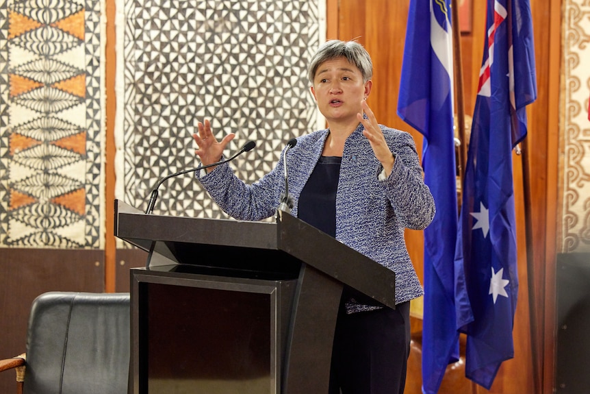 Penny Wong speaking behind a lectern in front of the Australian flag. 