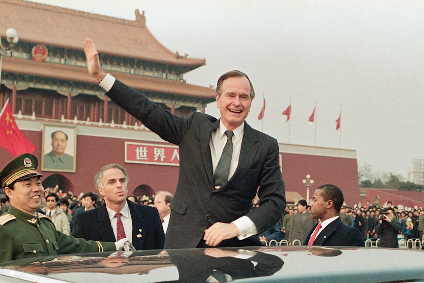 George HW Bush stands on a platform next to his motorcade waving to crowds in Beijing's Tianamen Square in 1989