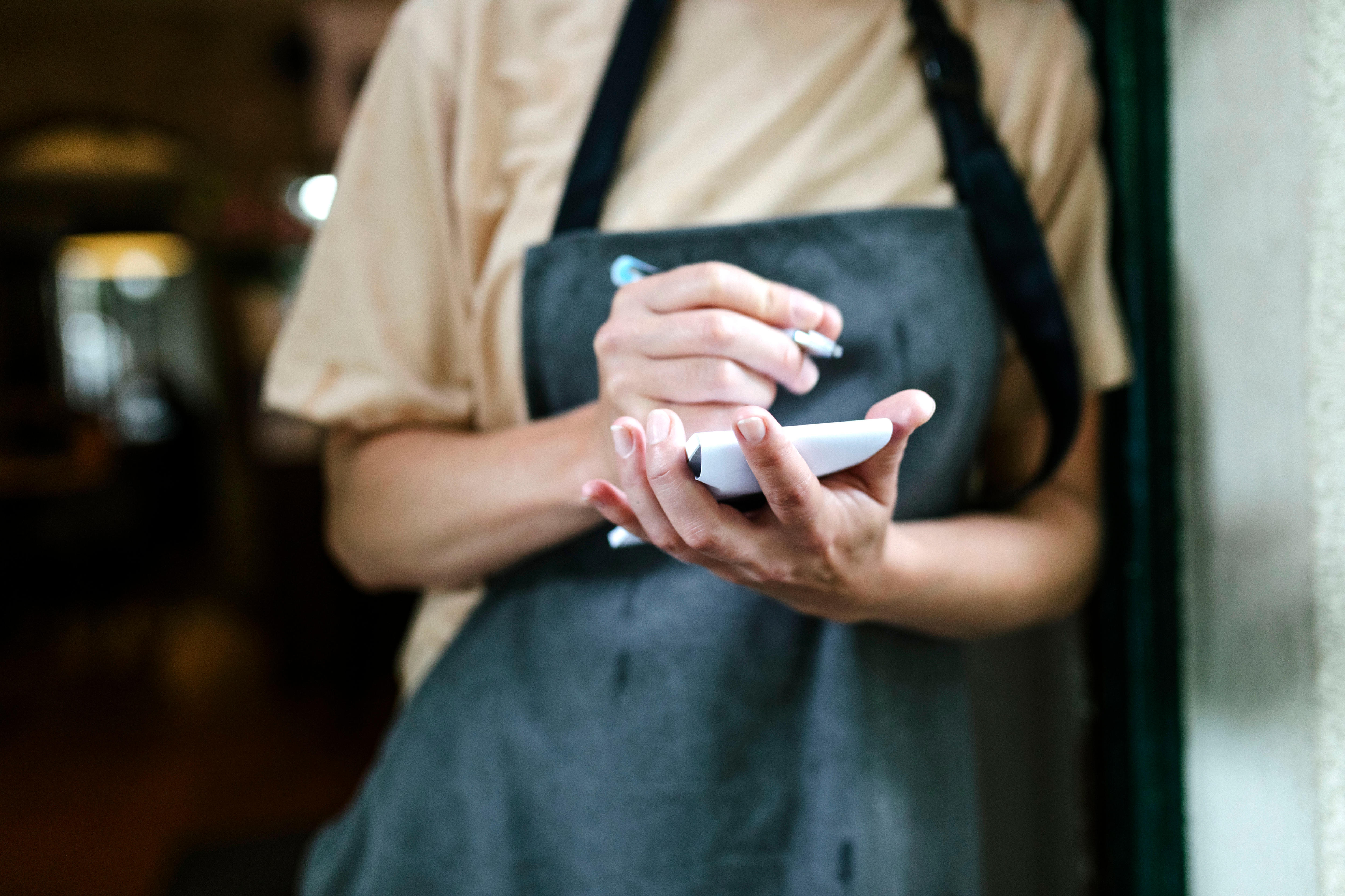 A torso of a waiter holding a notepad.