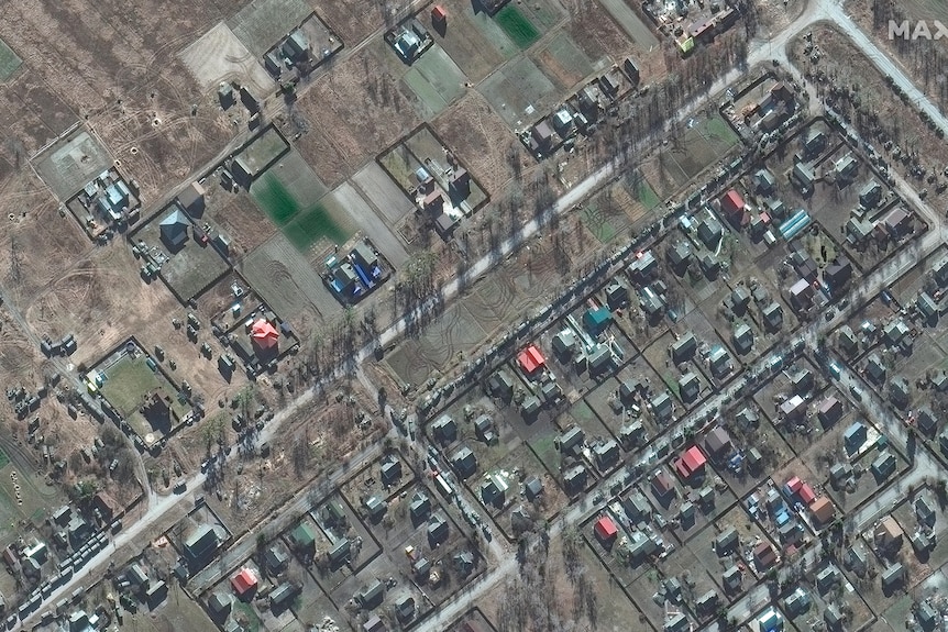 Satellite imagery shows village houses from above, with numerous military vehicles parked nearby