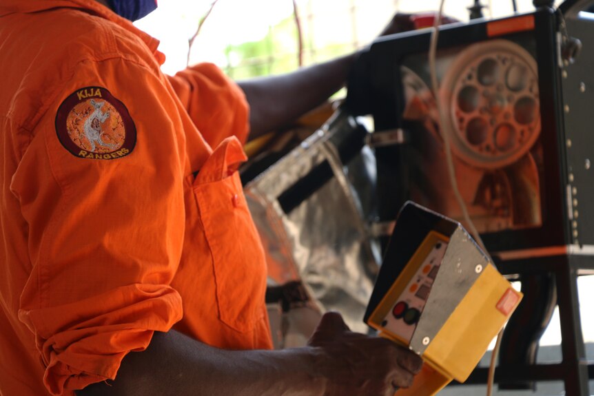 A closeup of a man's kija ranger's orange shirt while working. 