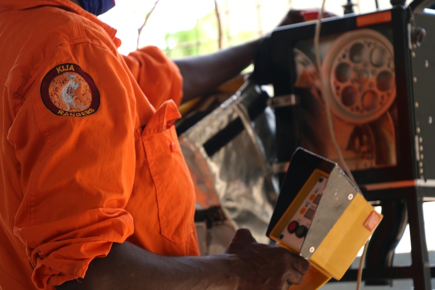 A closeup of a man's kija ranger's orange shirt while working. 