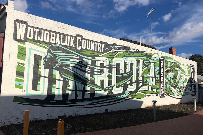 A green, white and black mural painted on side of a building that reads 'Wotjobaluk Country, Dimboola' with a river motif 