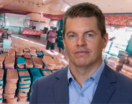 Un hombre con cabello corto y oscuro viste un traje oscuro mientras está a bordo de un barco.