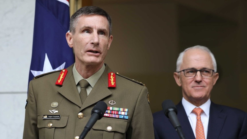 Angus Campbell, wearing his Army uniform, speaks into a microphone. Malcolm Turnbull stands beside him, smiling.