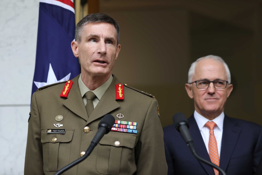 Angus Campbell, wearing his Army uniform, speaks into a microphone. Malcolm Turnbull stands beside him, smiling.