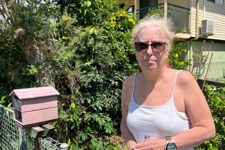 A woman in a tank top and sunglasses standing near her fence