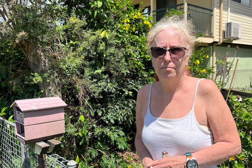 A woman in a tank top and sunglasses standing near her fence