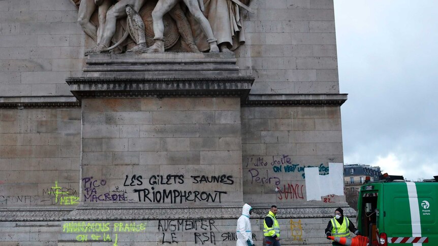 Parisian clean-up crews attend to the base of the graffitied Arc de Triomphe after riots