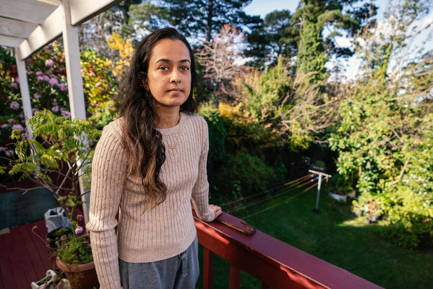 A woman with long hair stands outside on a balcony.