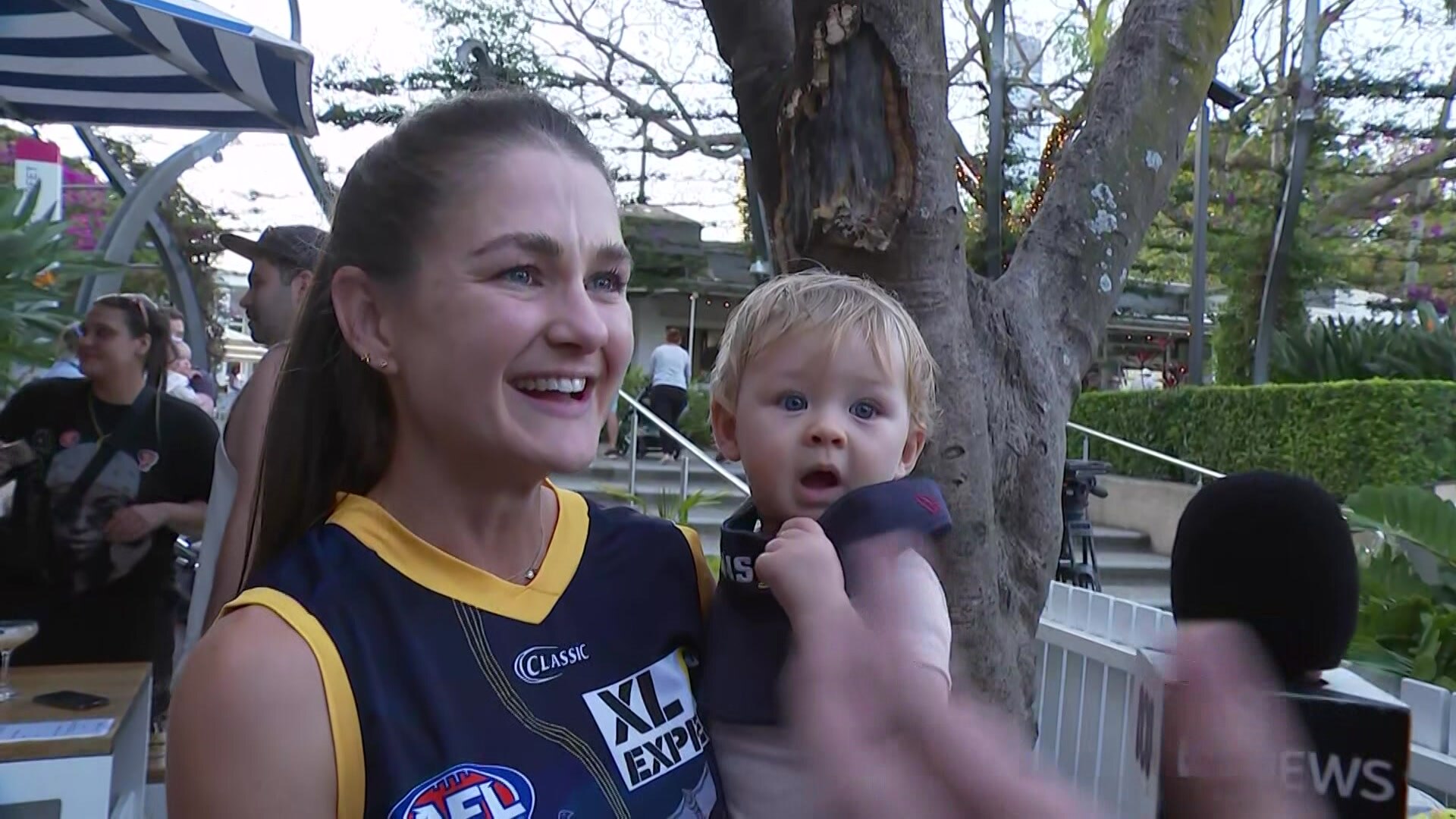 A woman in a Lions' jersey holding a baby.