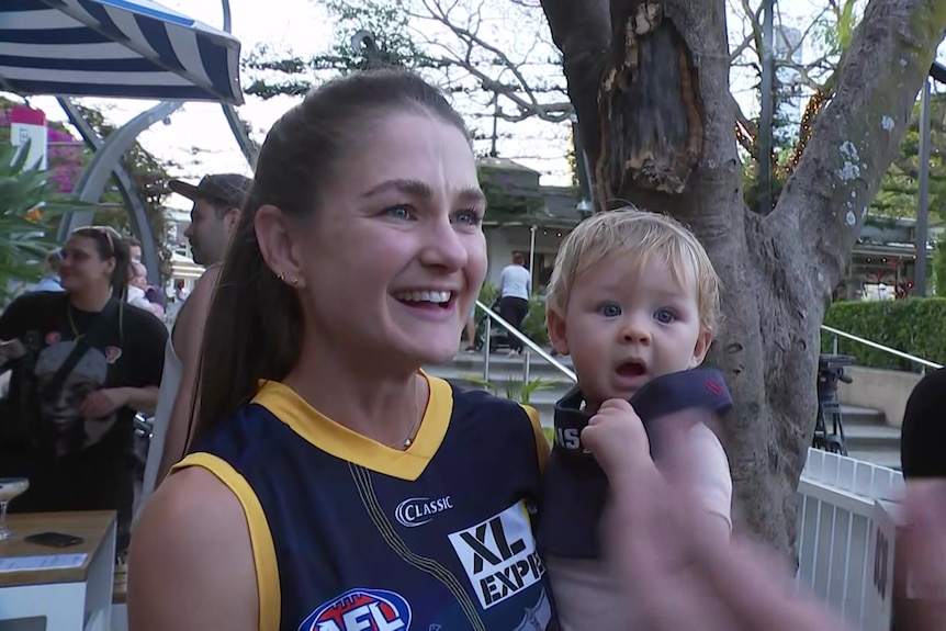 A woman in a Lions' jersey holding a baby.