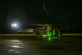 A green light shines out of a helicopter on wet tarmac at night