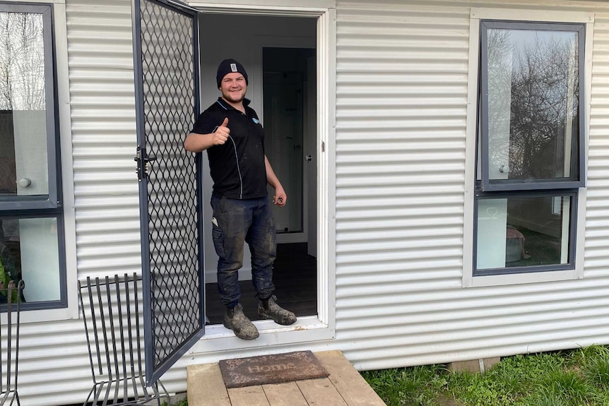 A smiling teen gives a thumbs up sign on the steps of a new building.