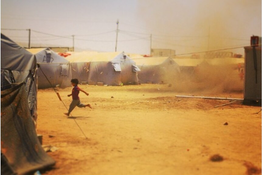 A boy runs from a sandstorm between tents in a refugee camp.