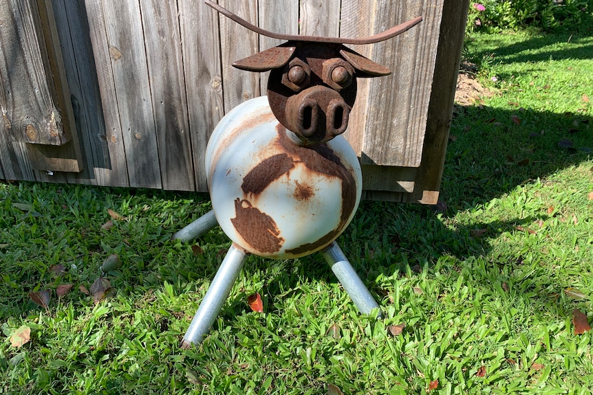 Cow sculpture made of rusty tin parts on the grass near a timber fence in cafe grounds