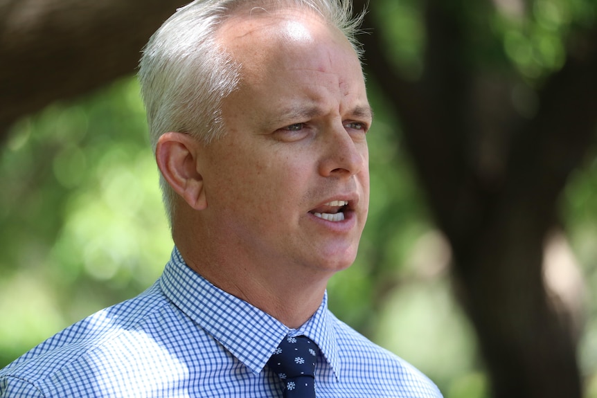 A formally dressed man with short white hair speaks to the media.