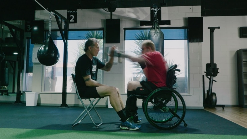 Professional boxer Danny Green (left) does boxing exercises with a young man in a red shirt in a wheelchair.