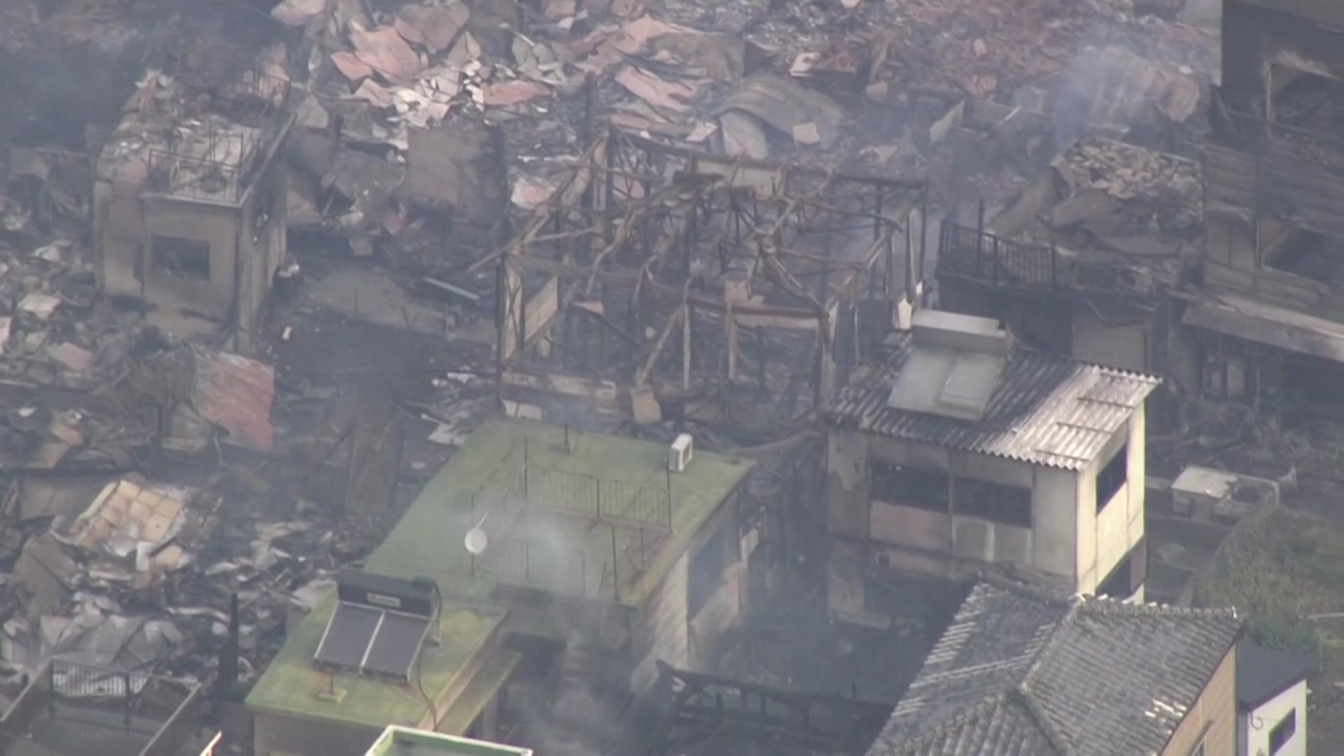 Aerial vision of burnt-out residential buildings, smoke billows.