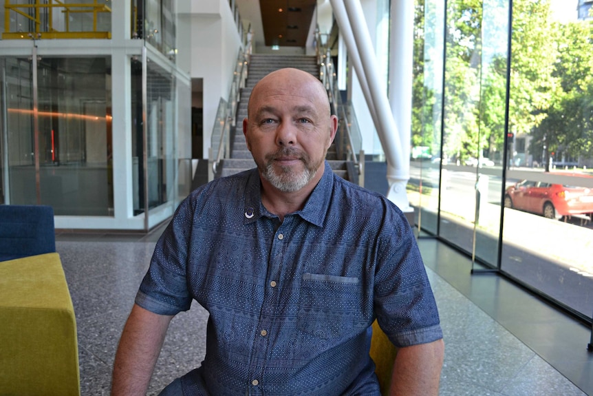 Gary Charnock sits on a couch and smiles at the camera.