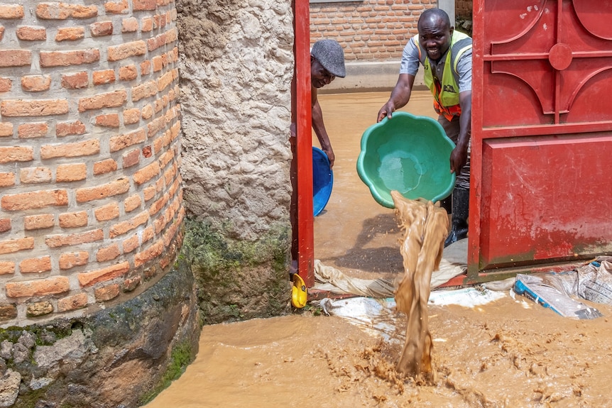 Residents drain water from their swamped home with a large bucket.