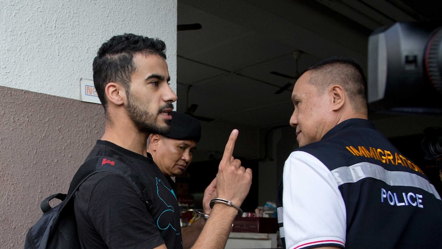 Bahraini football player Hakeem al-Araibi holds his finger up at a police officer