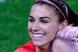 Alex Morgan jumps into the arms of Megan Rapinoe and both smile