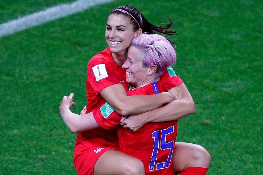 Alex Morgan jumps into the arms of Megan Rapinoe and both smile