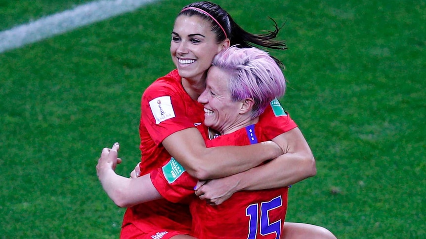 Alex Morgan jumps into the arms of Megan Rapinoe and both smile