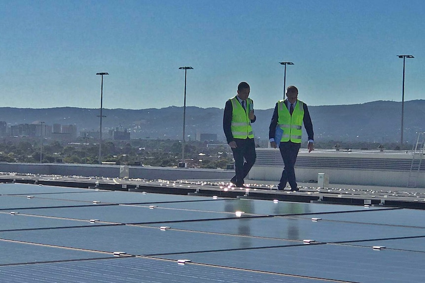 Tom Koutsantonis and Jay Weatherill inspect solar panels on a roof at Adelaide Airport.