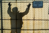 Man reaches for the top of a translucent fiberglass  fence while a sign on the other side warns of not trespassing.