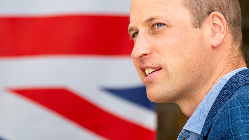 Prince William stands in front of the Union Jack flag.