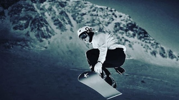 Winter Olympian Jarryd Hughes in the air on his snowboard after launching off some snow