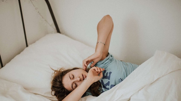A woman stretches in a bed with white sheets from above