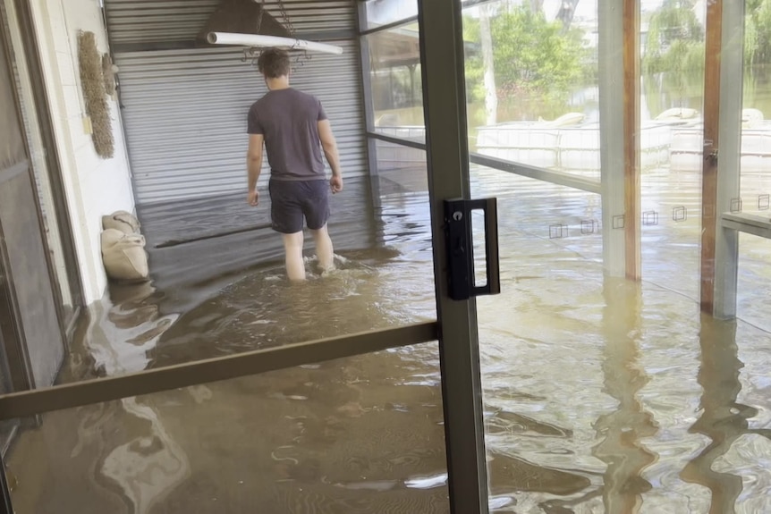 A man wading through knee-deep water in a flooded home.