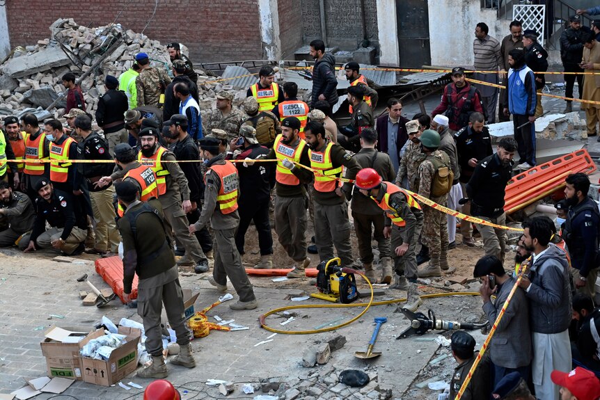 Security officials and rescue workers gather at the site of suicide bombing, near a pile of rubble.