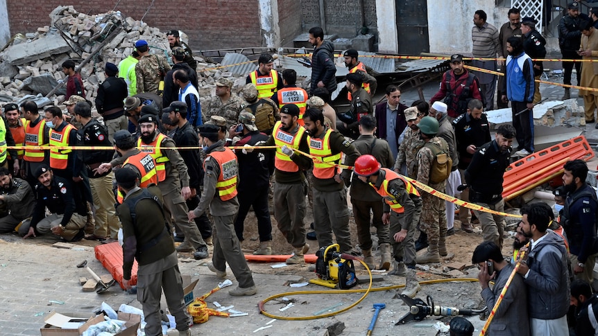 Security officials and rescue workers gather at the site of suicide bombing, near a pile of rubble.
