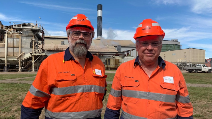 two men in hi vis in front of a sugar mill