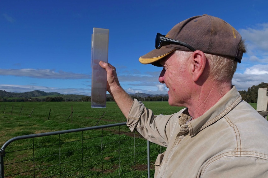A farmer holds up a rain gauge with water in it.