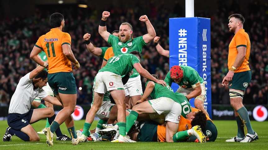 An Irish rugby player pumps his fists in triumph as a referee kneels and raises his arm to signal a try against Australia. 