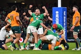 An Irish rugby player pumps his fists in triumph as a referee kneels and raises his arm to signal a try against Australia. 