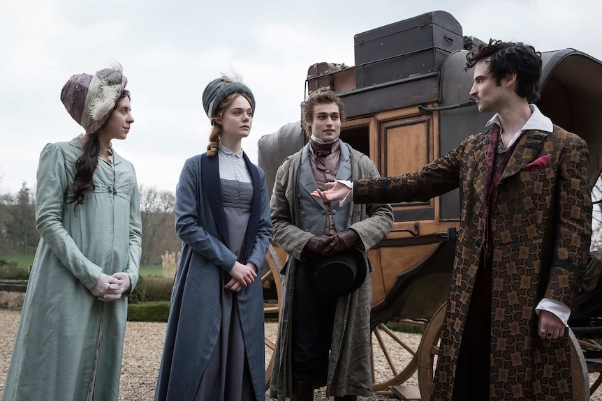 The four actors, all in 19th century garb, stand in conversation in front of a stage-coach.