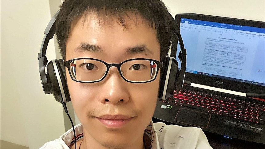 Teacher Victor Sun at home with his computer and headphones which he uses to teach St Johns students