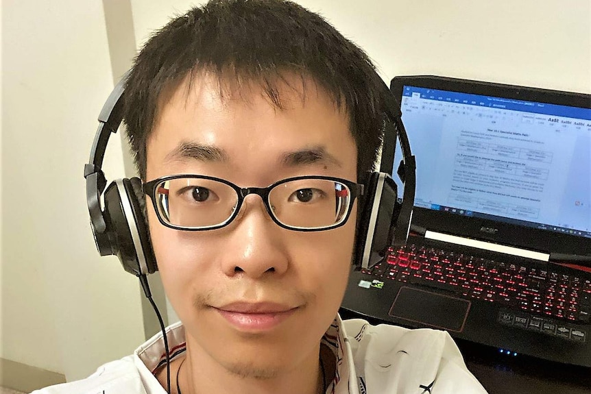 Teacher Victor Sun at home with his computer and headphones which he uses to teach St Johns students