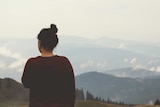 A woman stands alone in contemplation, looking out at snow capped mountains.